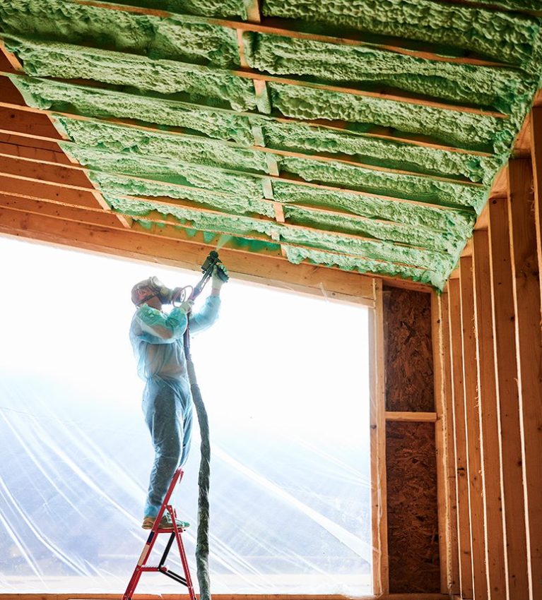 Worker spraying polyurethane foam for insulating wooden frame house.
