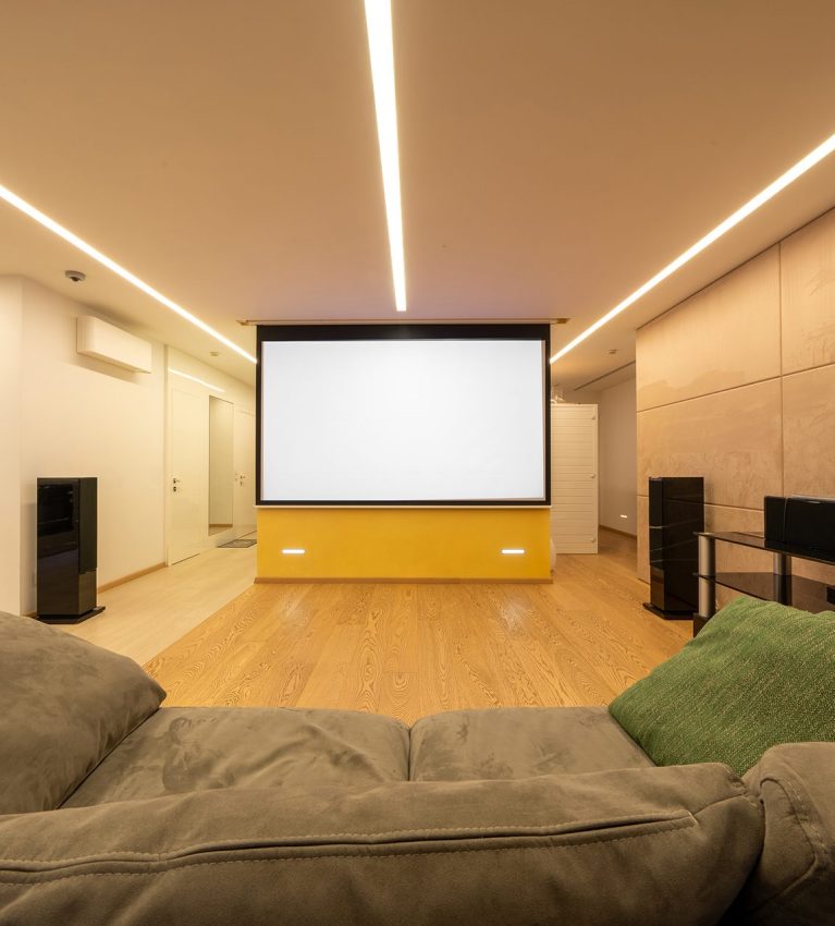 Big, gray sofa standing on beige wooden floor of a bright, luxurious living room interior with elegant elements and large TV. Stock photo